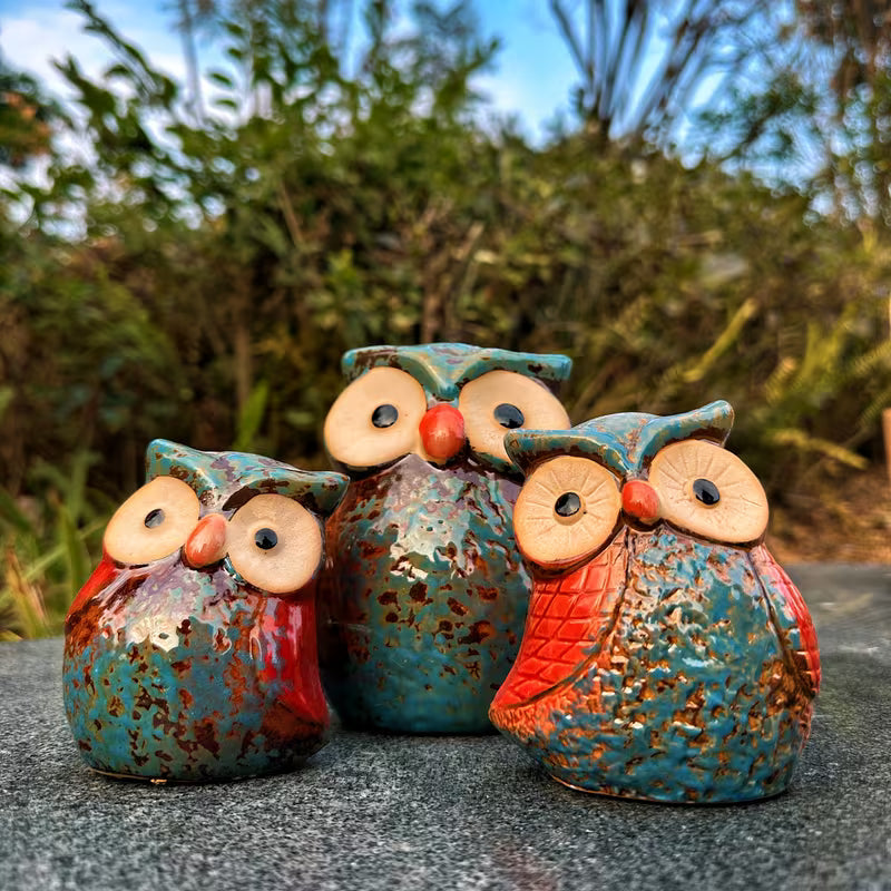 Drie uilen beeldjes op een steen in de tuin met groen op de achtergrond