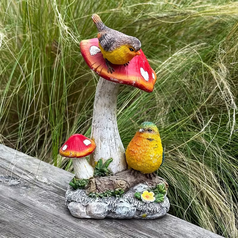 Paddenstoel tuinbeeld met twee vogels tussen klimop en gevallen bladeren, met een vogeltje op de rode hoed en een tweede aan de voet
